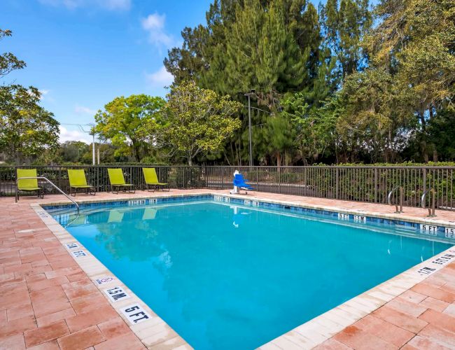 Outdoor swimming pool, blue water, lounge chairs, surrounding trees, clear sky.