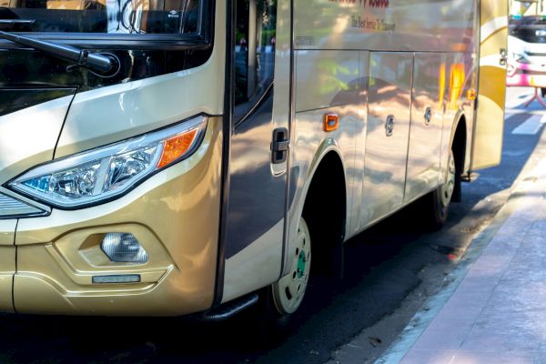 A close-up view of a parked bus with a shiny, beige exterior, reflecting sunlight on a city street.