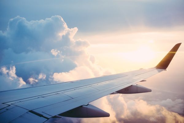 An airplane wing flying above the clouds with a beautiful sunrise or sunset in the background, illuminating the scene with warm colors.