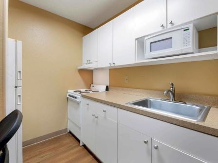 A small kitchen with white cabinets, a microwave, a stove, a sink, and a refrigerator. It has wooden flooring and beige walls.